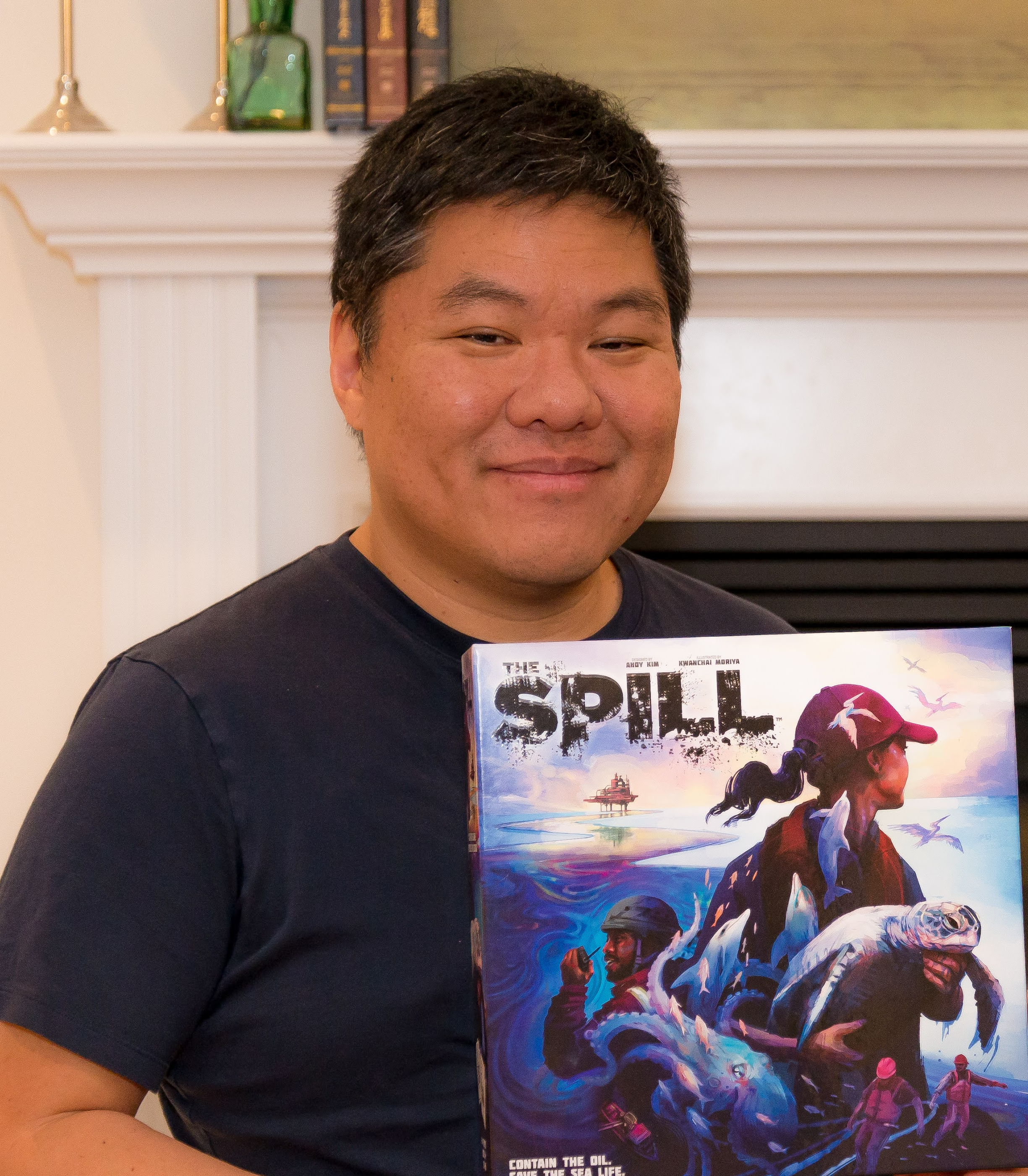 Andy Kim smiling at the camera holding a copy of his game The Spill