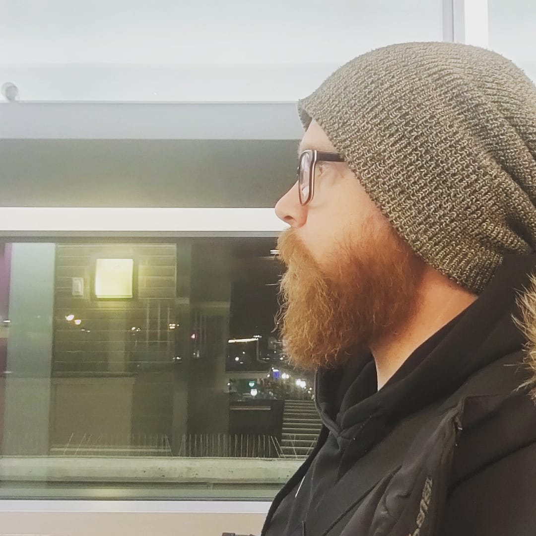 Brent Logan, a bearded man with glasses, wears a toque and looks thoughtfully into the distance