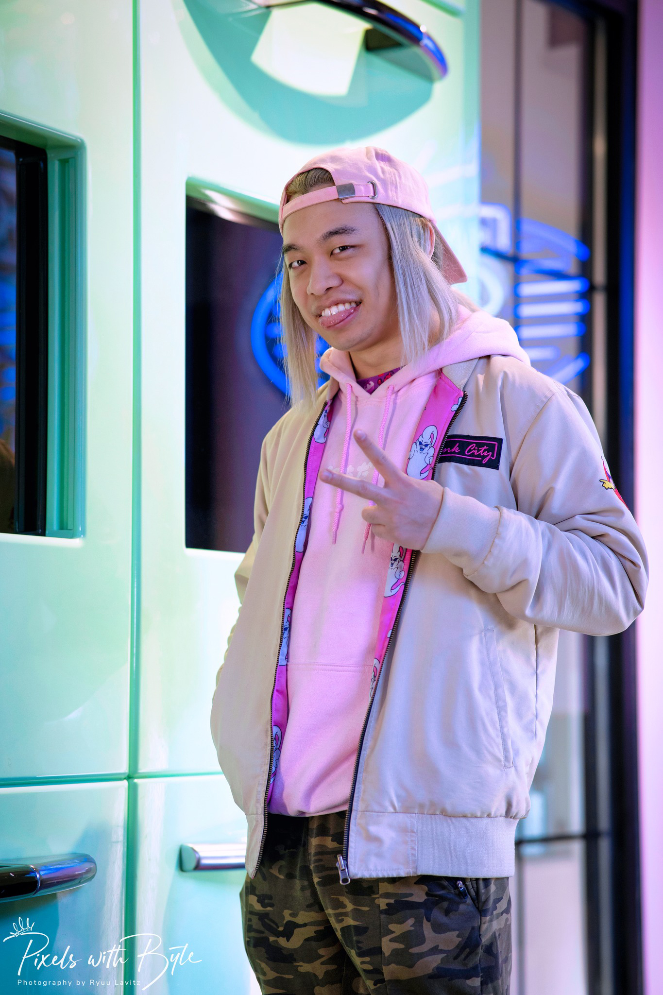 Chris Tung, in a vibrant pink Pink City branded hoodie, flashes a casual smile with a reverse peace sign