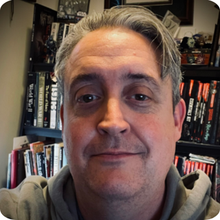 Head shot of Bill Benham standing in front of a bookshelf.