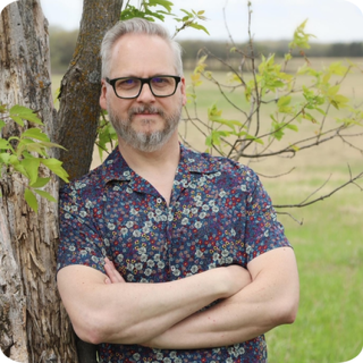 Greg Leatherman standing, leaning against a tree.