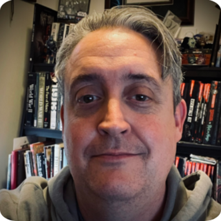 Head shot of Bill Benham standing in front of a bookshelf.