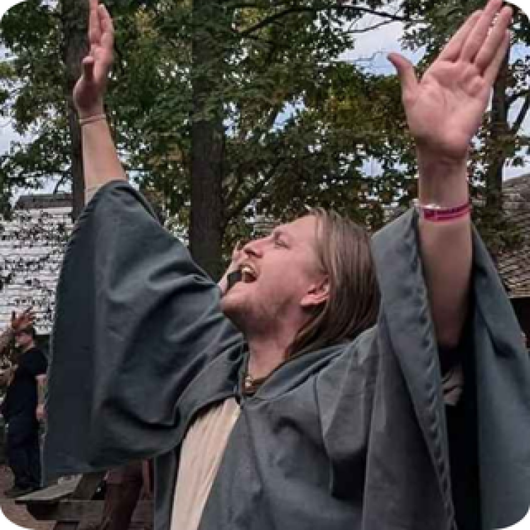 Ric Heise with his arms raised wearing a cloak. 